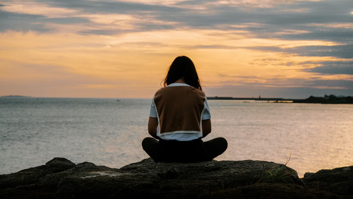 A serene scene of a woman sitting on rocks by the sea during a vibrant sunset.