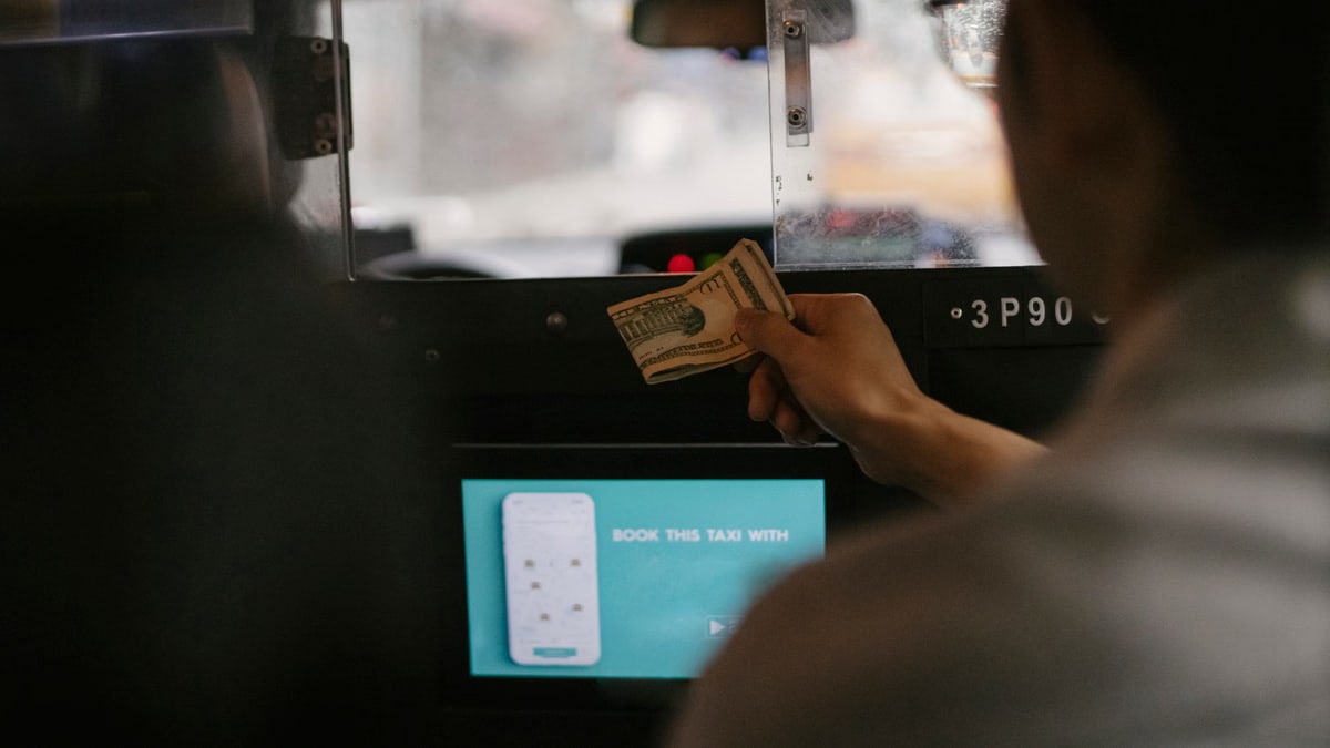 Back view of taxi car interior with tablet screen located near passenger seat and client paying for ride